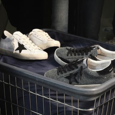 white-superstar-sneaker-and-grey-glittered-superstar-sneaker-in-metal-basket-on-top-of-navy-blue-fabric