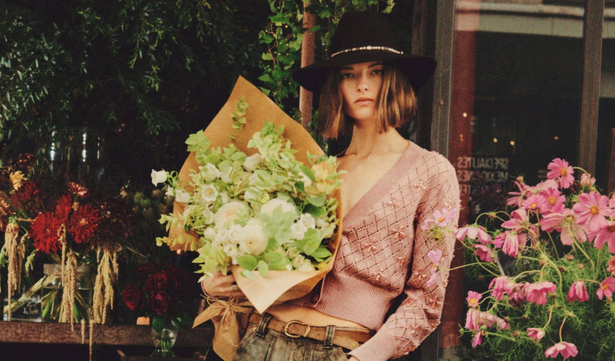 model-with-a-hat-and-a-pink-cropped-cardigan-holding-a-bouquet-of-colourful-flowers
