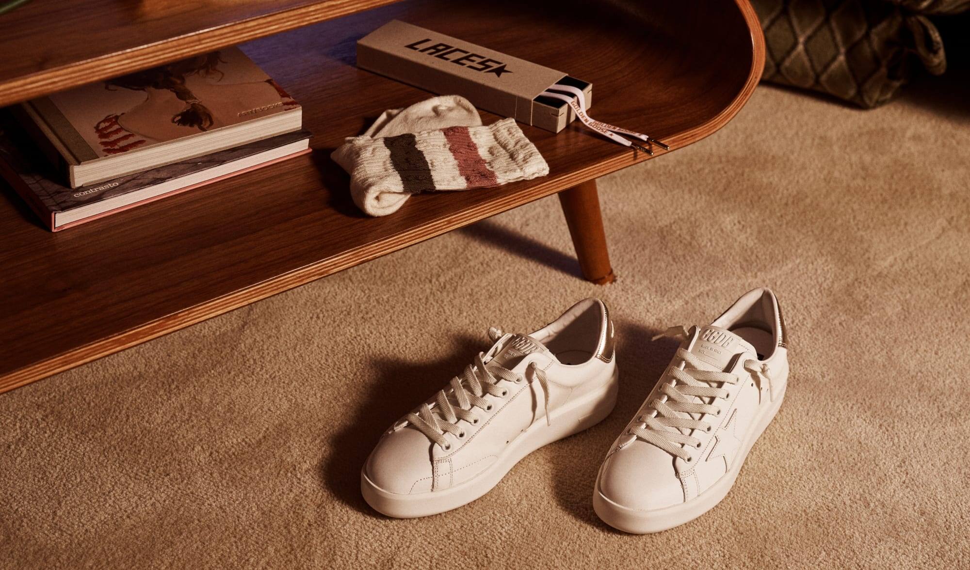 white-pure-star-sneakers-on-beige-moquet-under-wooden-table-with-books-socks-and-laces-on-bottom-shelf
