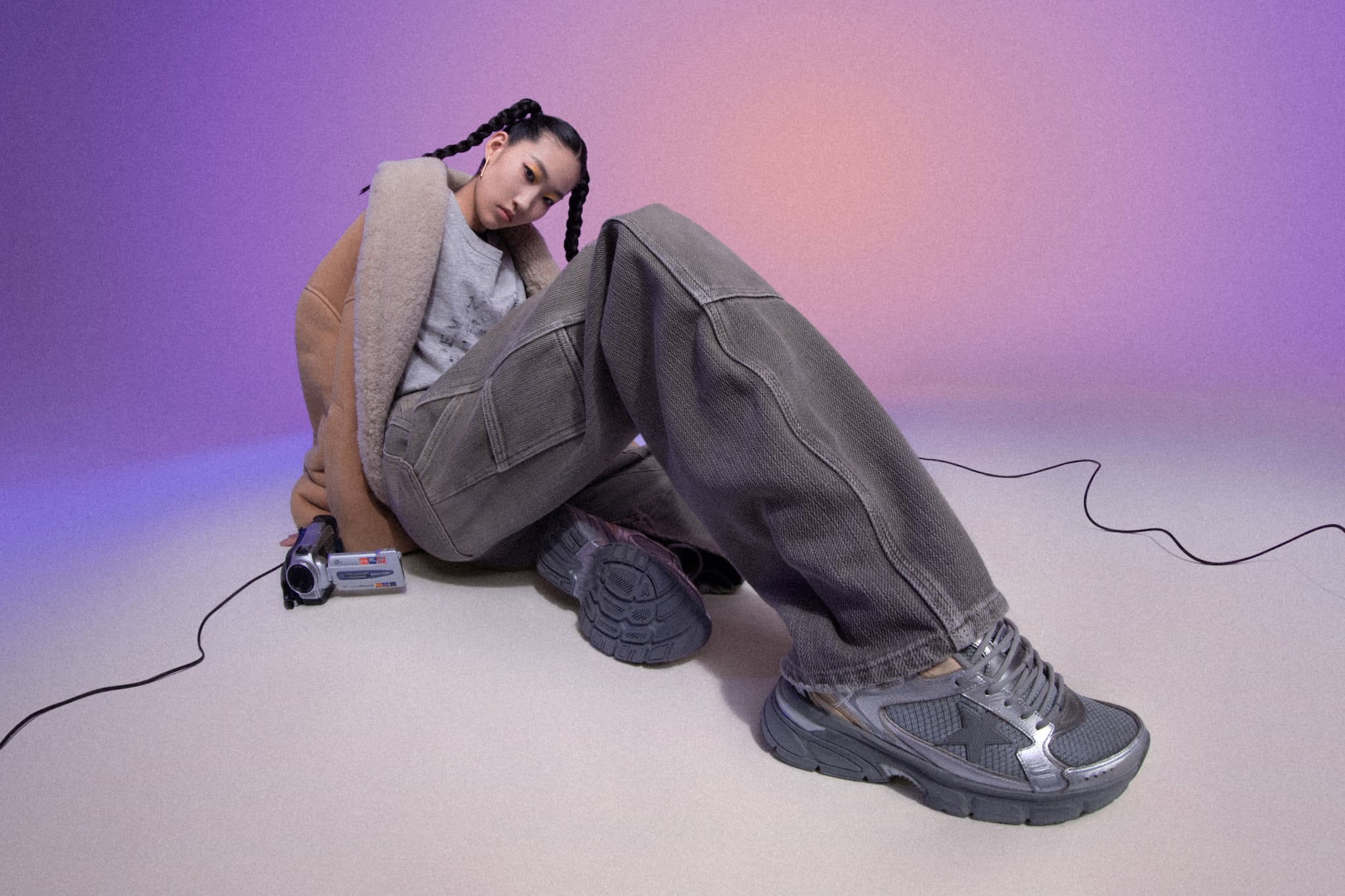 Asian woman wearing silver lightstar sneakers laying on floor next to old video camera