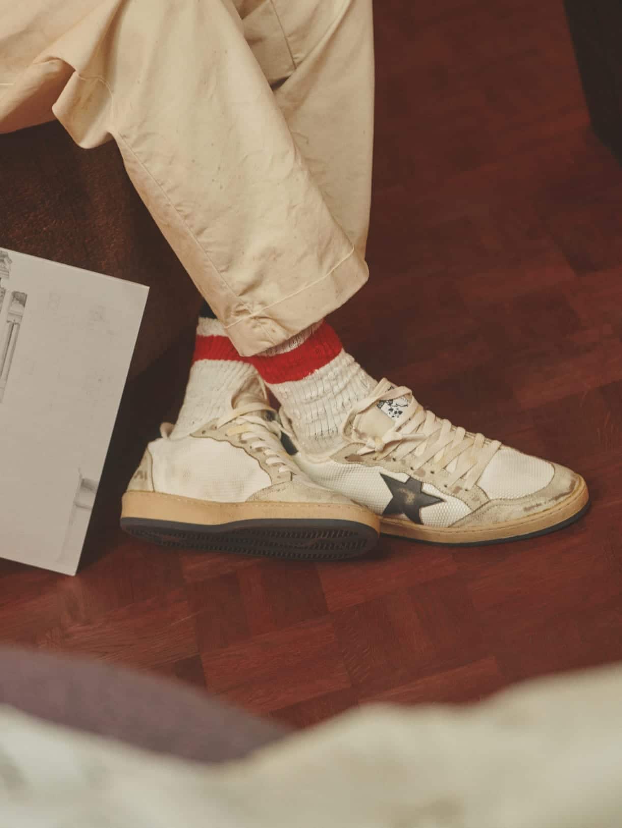 white-ball-star-sneakers-with-black-star-with-white-and-red-socks-and-beige-pants-on-wooden-parquet-floor