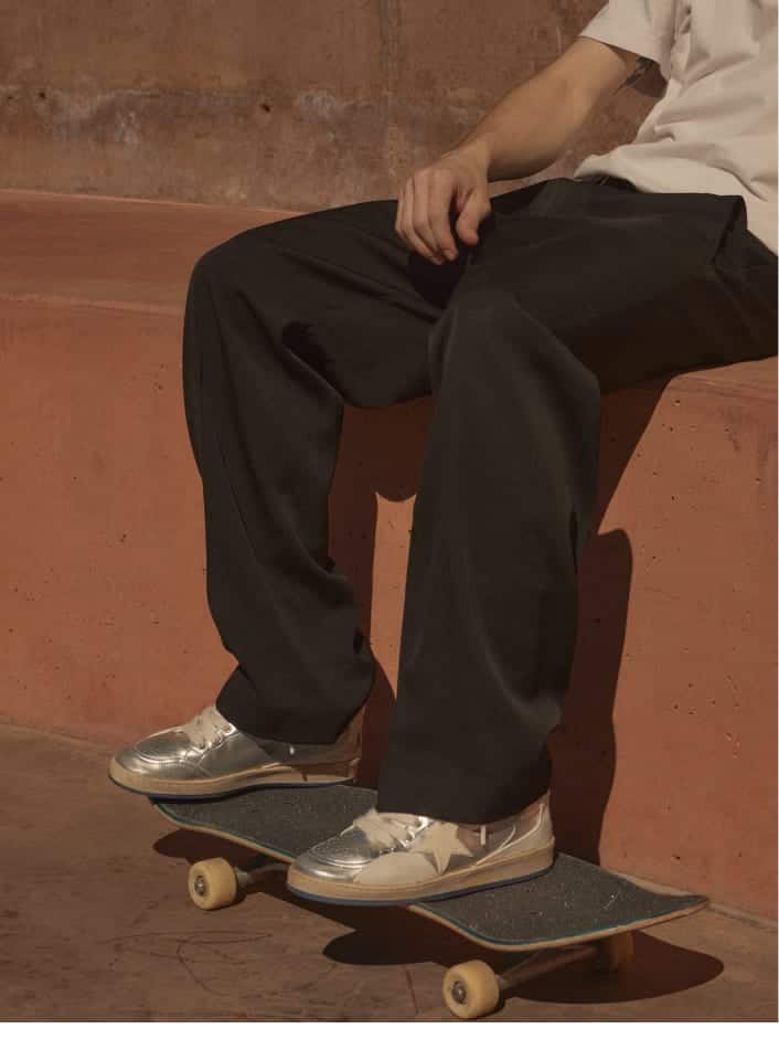 side-view-of-black-pants-and-silver-ball-star-pro-sneakers-on-skatebord-while-sitting-on-brick-red-edge
