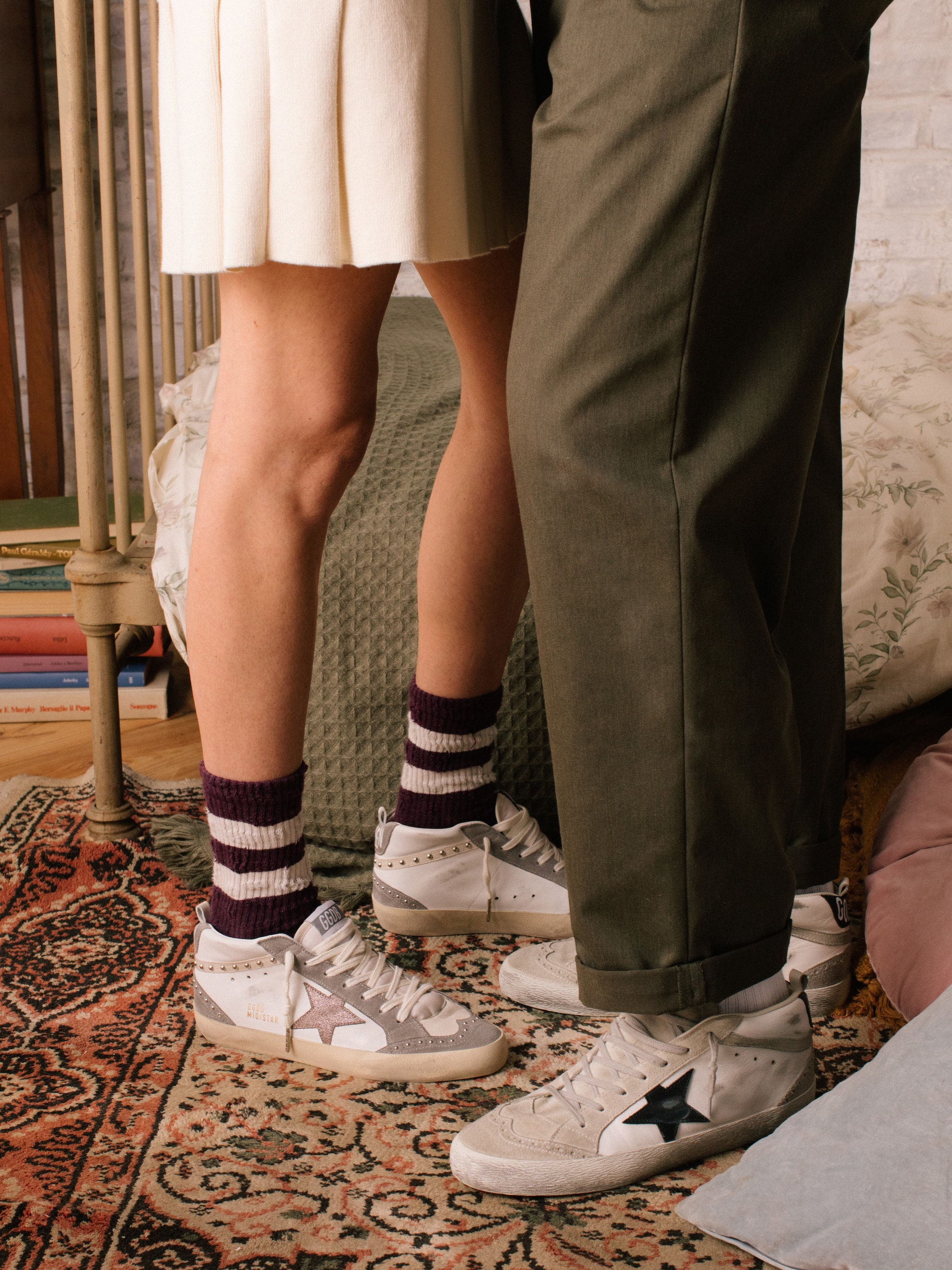 Striped-socks-and-white-midstar-sneakers-on-a-persian-rug-and-a-couple-on-the-background-laying-on-a-bed