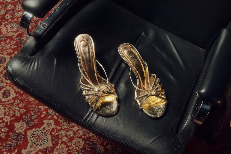 pair-of-golden-heeled-sandals-shoes-on-a-blcak-leather-chair