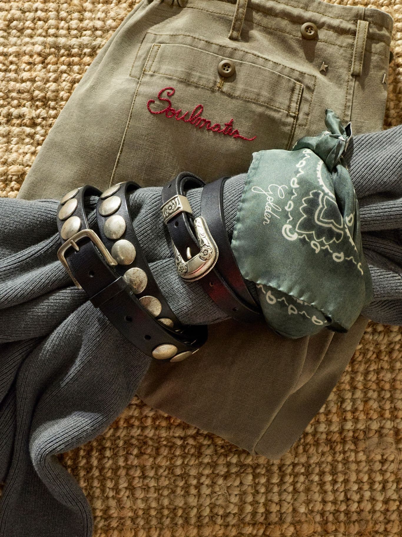 black-leather-belt-with-studs-rolled-up-over-a-blue-sweater-with-a-green-scarf-over-green-trousers