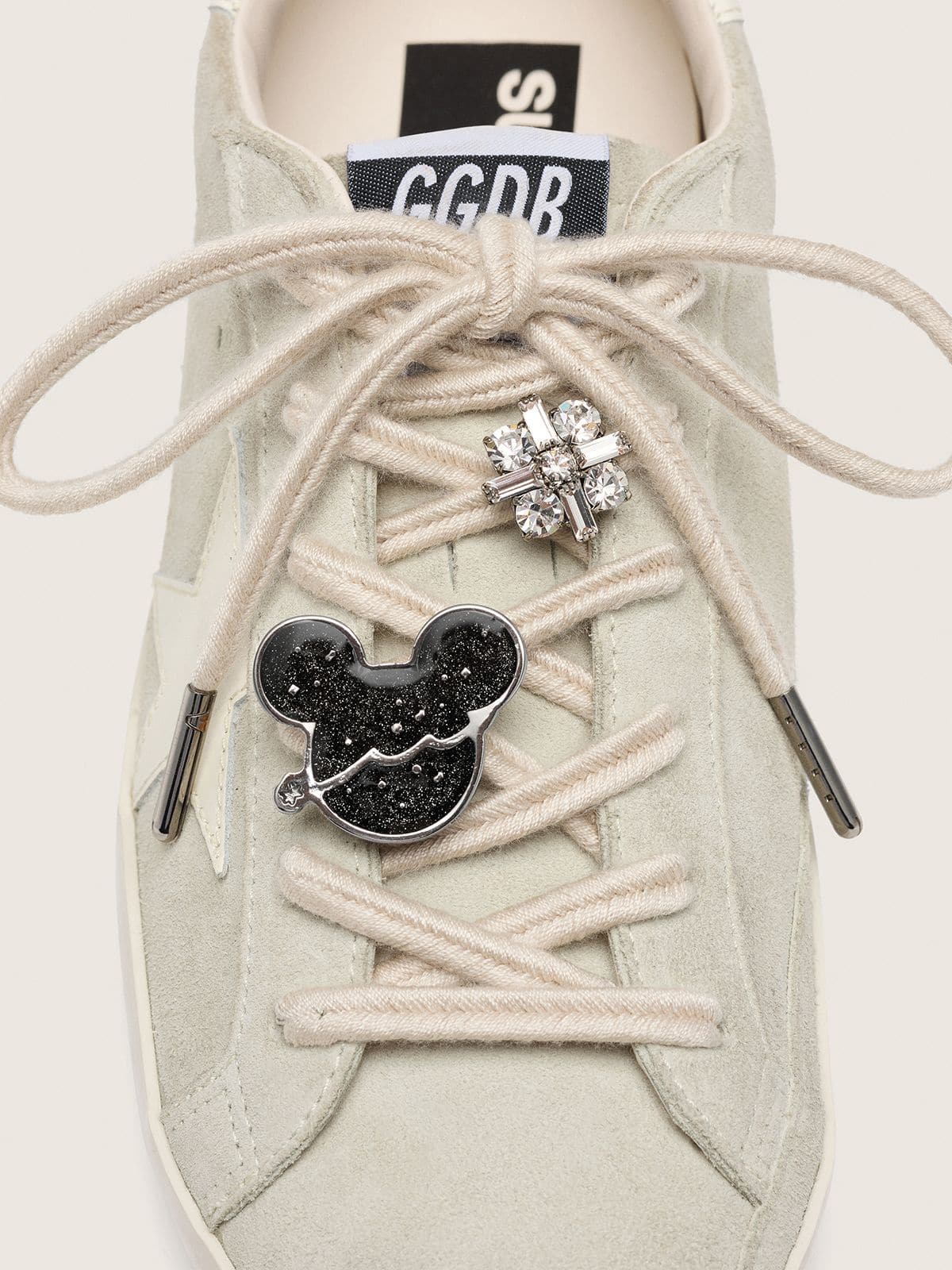 Disney | Golden Goose Skins cord&oacute;n trenzado beige con un pin y un charm